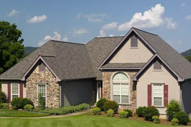 A house with a spacious yard and a prominent, large roof, showcasing a welcoming suburban environment.