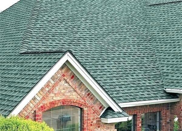 A house with a distinctive green roof and brick detailing, highlighting roofing services offered