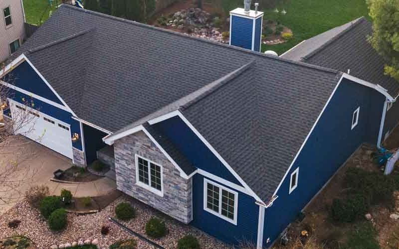 A blue house featuring a gray roof and a paved driveway in front.