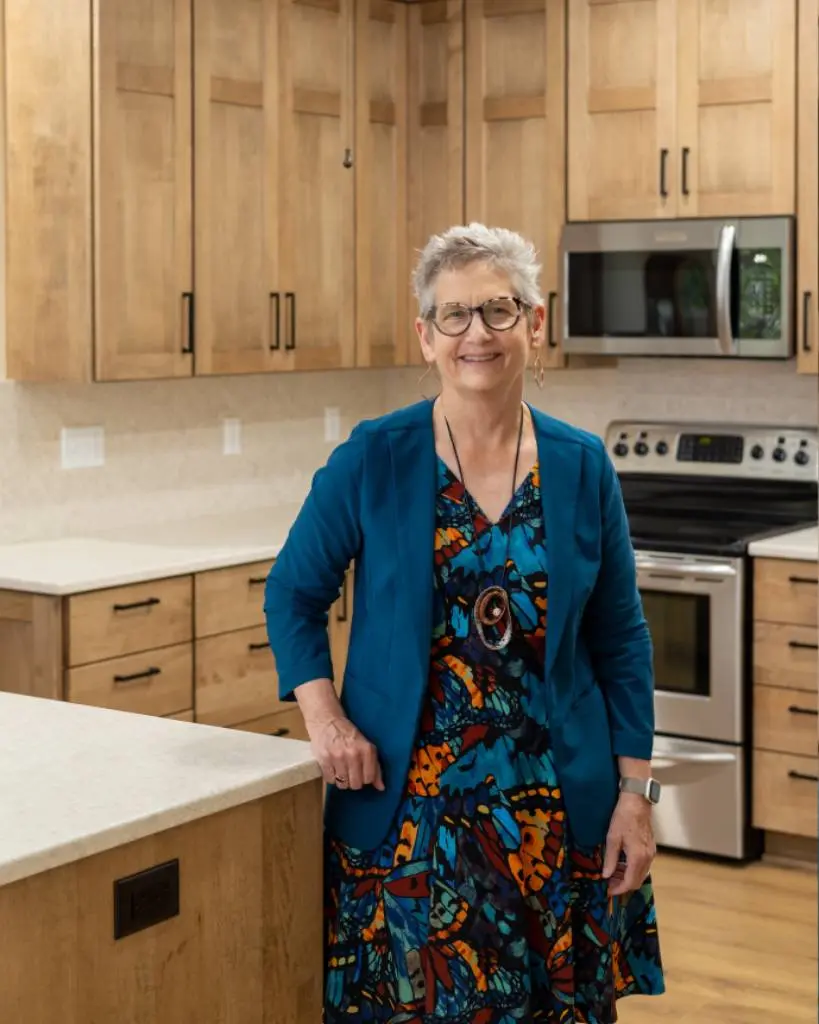 Dondi Szombatfalvy stands in a modern kitchen with wooden cabinets and stainless steel appliances.