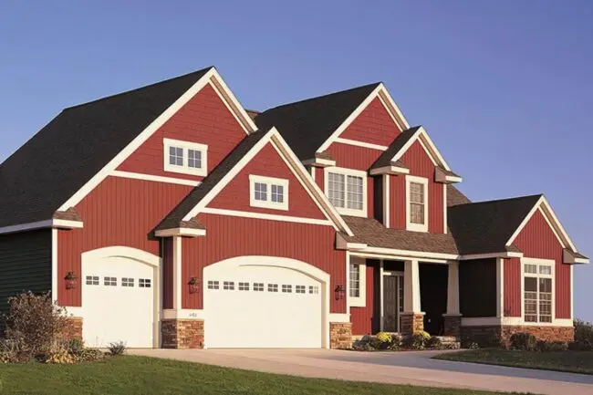 A charming red and white house with an attached garage, surrounded by greenery.