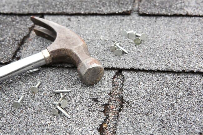 A hammer and screws placed on a roof, indicating roofing work related to gutters and insulation services