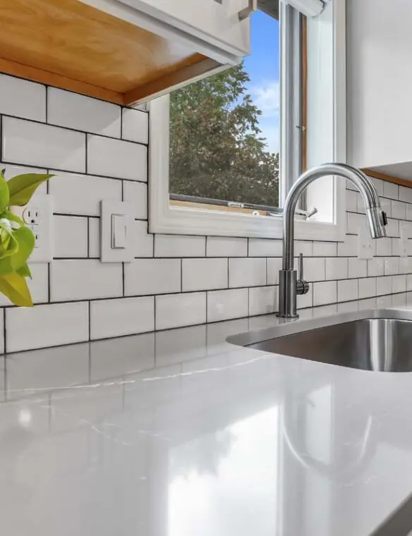 A modern kitchen featuring white subway tile walls and a stainless steel sink.