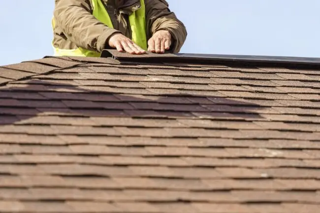 A man working on a house roof, demonstrating skilled roofing services being performed
