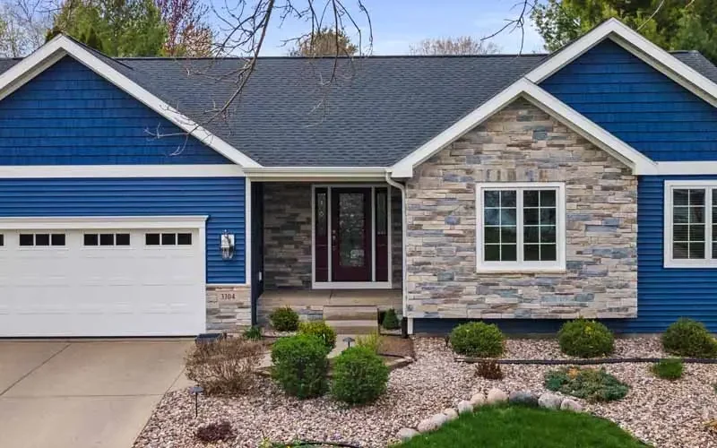 A blue house with stone siding and a vinyl garage, showcasing a modern architectural design.