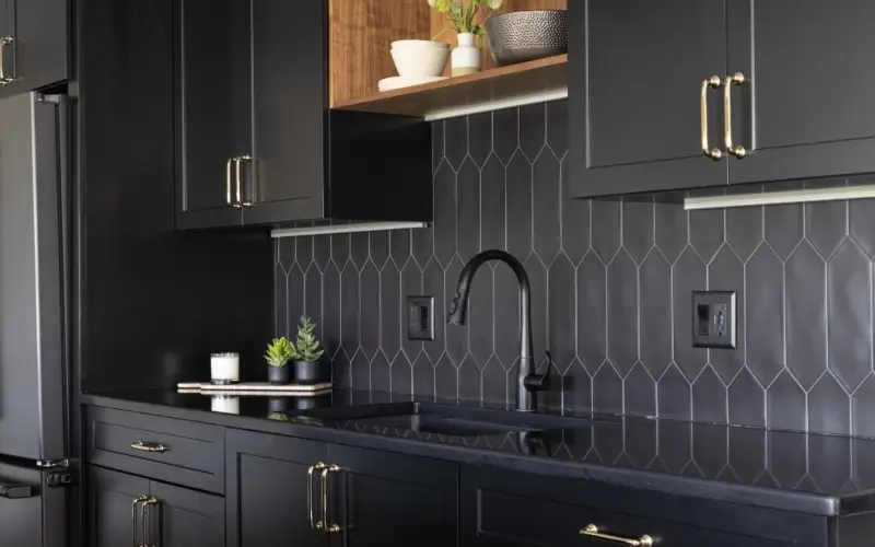 Chic black kitchen design with gold accents and black cabinets, featuring a contemporary Kohler Simplice faucet.