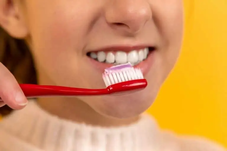 What is a Cavity? Edina Dentist Explains 8 Woman brushing front teeth with red toothbrush and smiling.