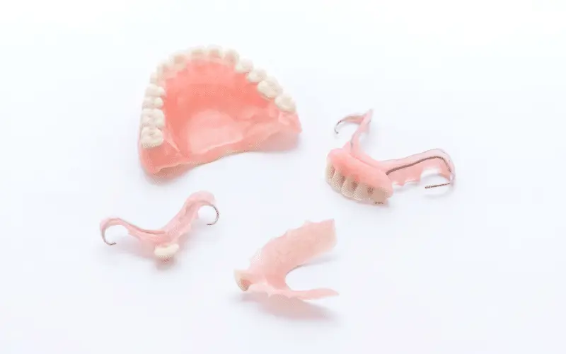 Multiple types of pink acrylic removable dentures laid on white background.