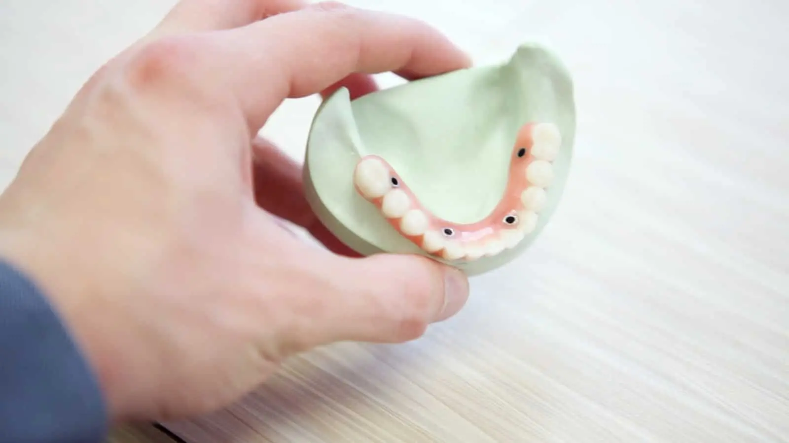 Hand holding dental mold with partial denture attached.