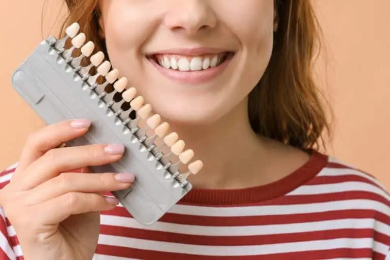 Young woman holding tooth shade guide and smiling.