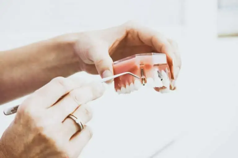 Hand holding clear aligner tray above dental mold.