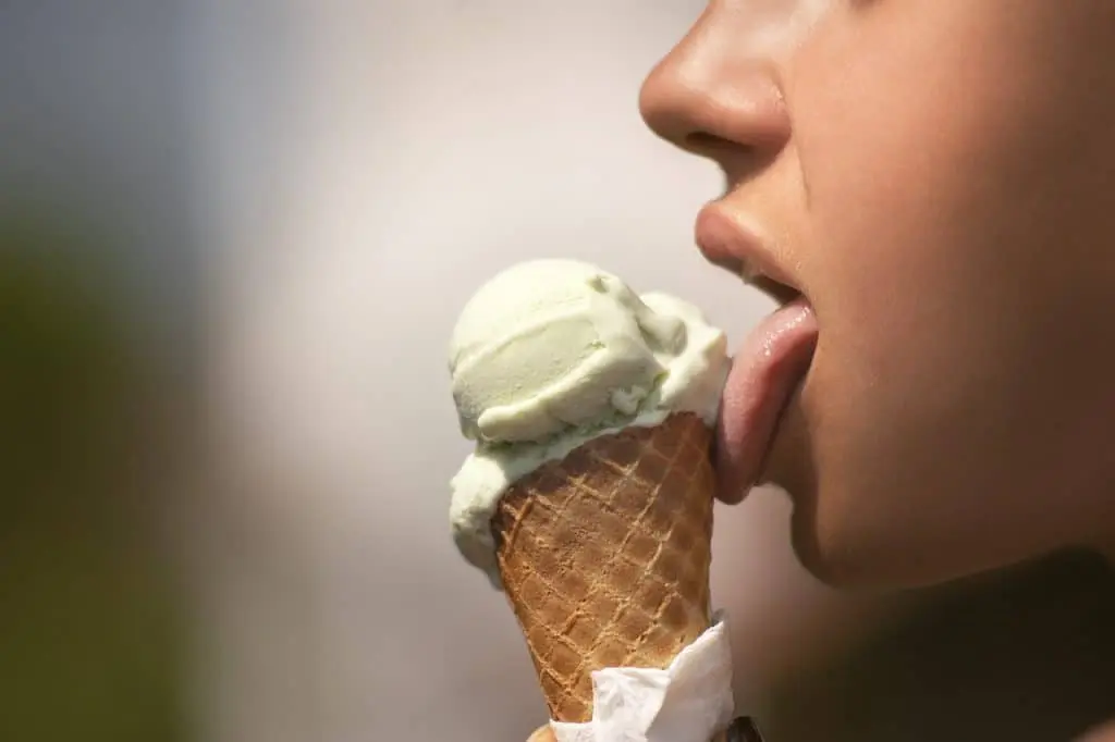 Person eating ice cream cone with sensitive front teeth exposed.
