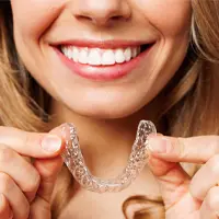 Home 4 Person smiling, holding Invisalign in both hands.