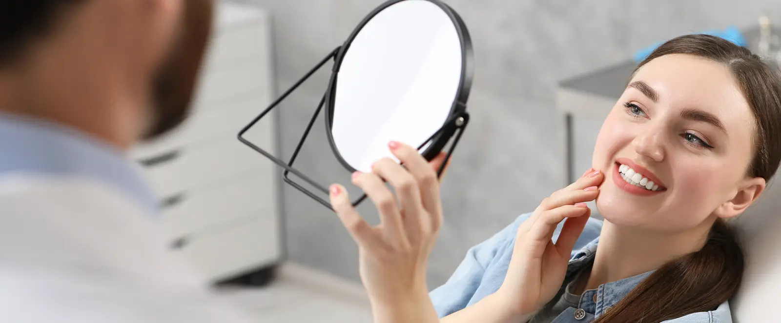 Home 1 Woman adjusting her smile while holding a mirror, showing the importance of a top-rated dentist in Westbury, NY