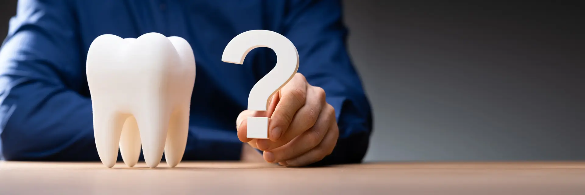 FAQs 1 A man displays a tooth marked with a question mark, representing questions or concerns regarding dental issues.