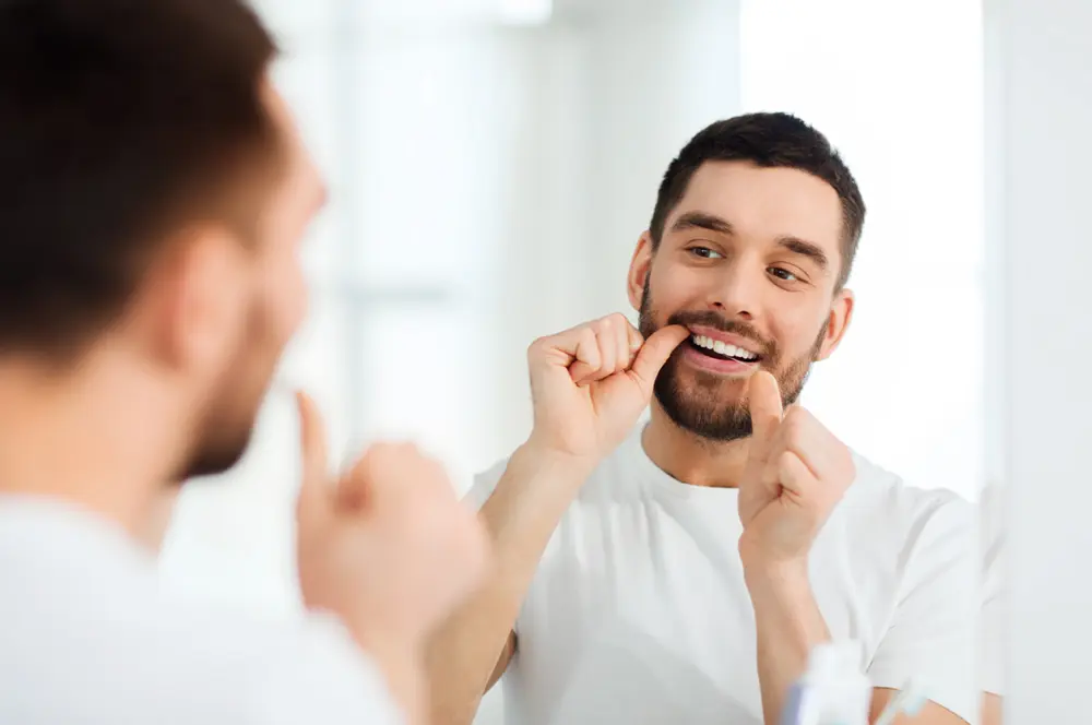 Cavity Prevention | VP Dental | Cavity Prevention A man flossing his teeth in front of a bathroom mirror, promoting cavity prevention.