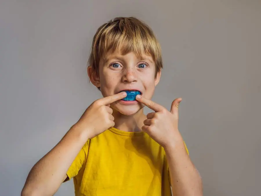 Myobrace | VP Dental | Myobrace in Raleigh A young boy in a yellow shirt pointing to a blue Myobrace appliance in his mouth