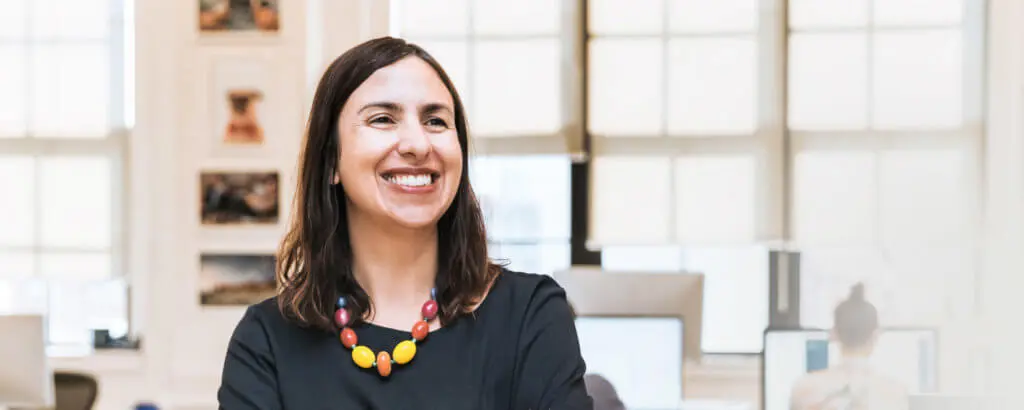 Mercury-Safe And Mercury-Free | VP Dental | Mercury-Free Dentistry in Raleigh Smiling woman wearing a colorful necklace, standing in a dental office