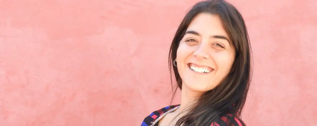 Scaling and Root Planing | VP Dental | Scaling and Root Planing A woman smiling with healthy teeth standing against a pink wall, representing the benefits of scaling and root planing