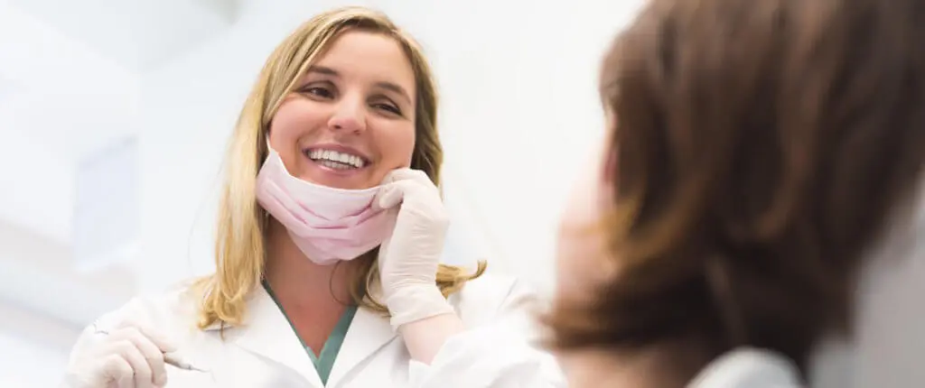 A dentist lowering her mask while speaking to a patient during a periodontal cleaning.