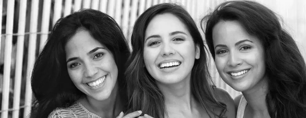 Three young women with straight, bright smiles posing together, highlighting orthodontic results