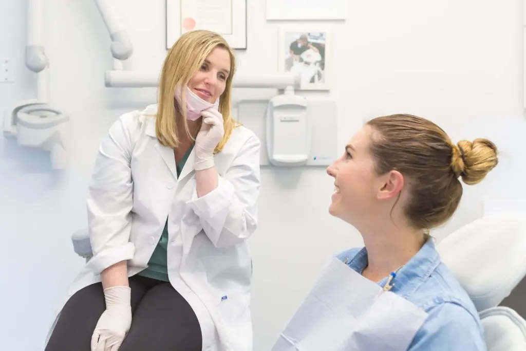 FAQs | VP Dental | Dental FAQ Dentist in a white coat talking to a smiling patient in a dental chair