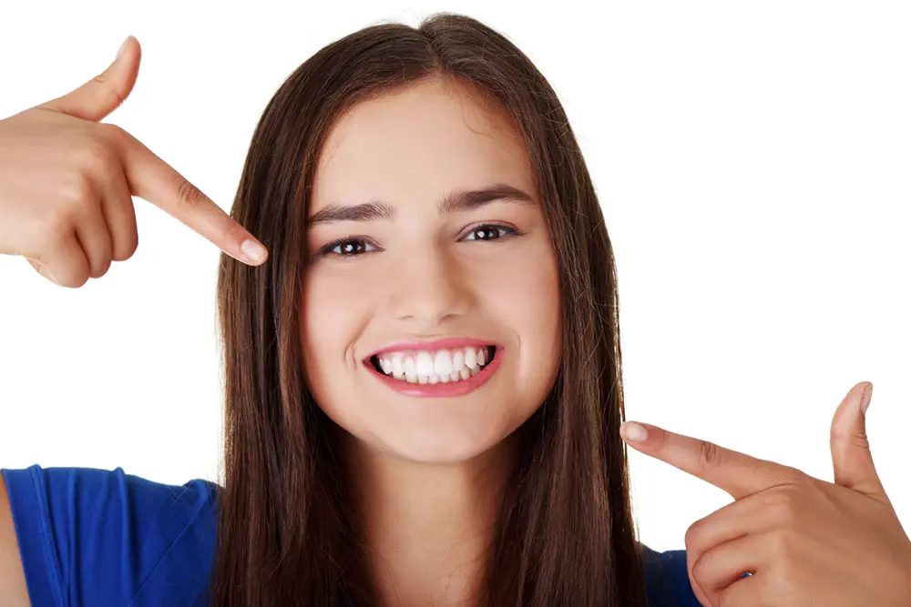 A young woman pointing to her healthy teeth, representing the benefits of myofunctional therapy