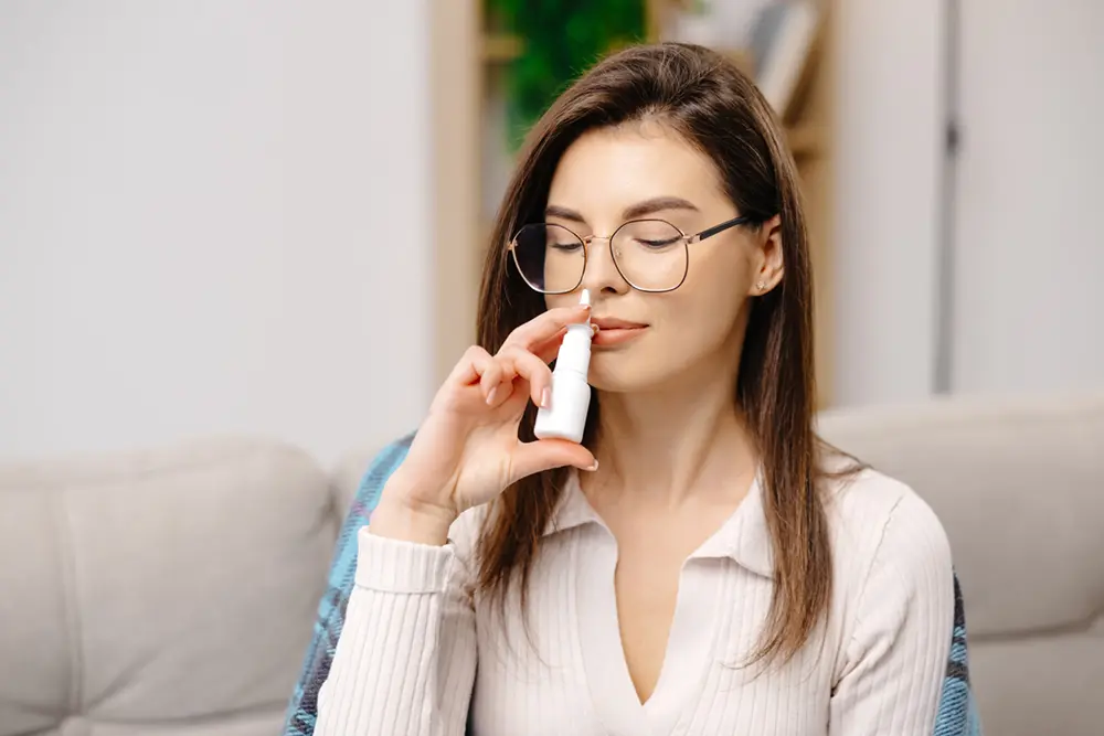 Xlear Nasal Spray | VP Dental | Xlear Nasal Spray in Raleigh A woman sitting on a couch using Xlear nasal spray, with a relaxed expression