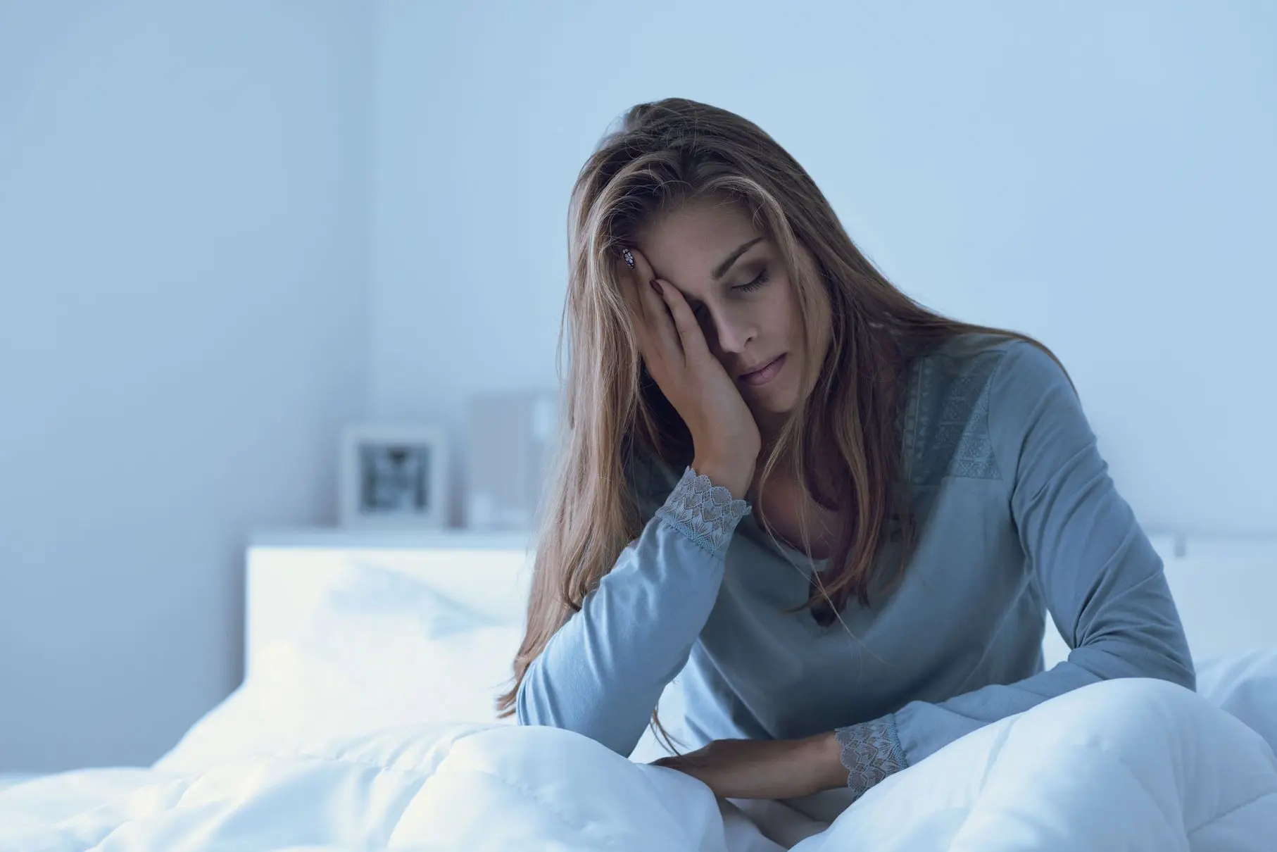 A tired woman sitting on her bed, representing the exhaustion caused by sleep apnea