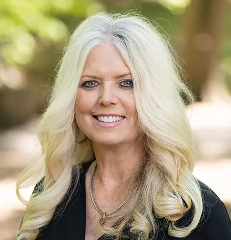 Head shot of Beth, Scheduling Coordinator, smiling warmly in a black top with her blonde hair