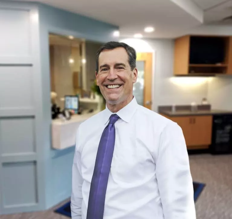Dr. Nordone wearing a white shirt and purple tie stands in a brightly dental office space 