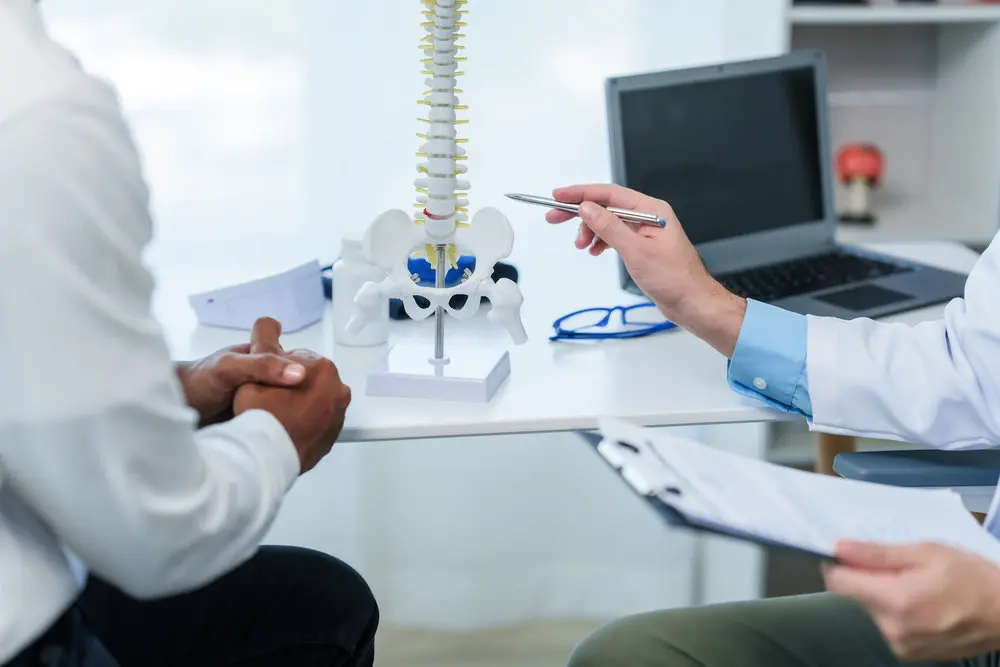 Close up male doctor and patient people in a medical office, spine model, possibly discussing spinal condition or syndrome with the patient.
