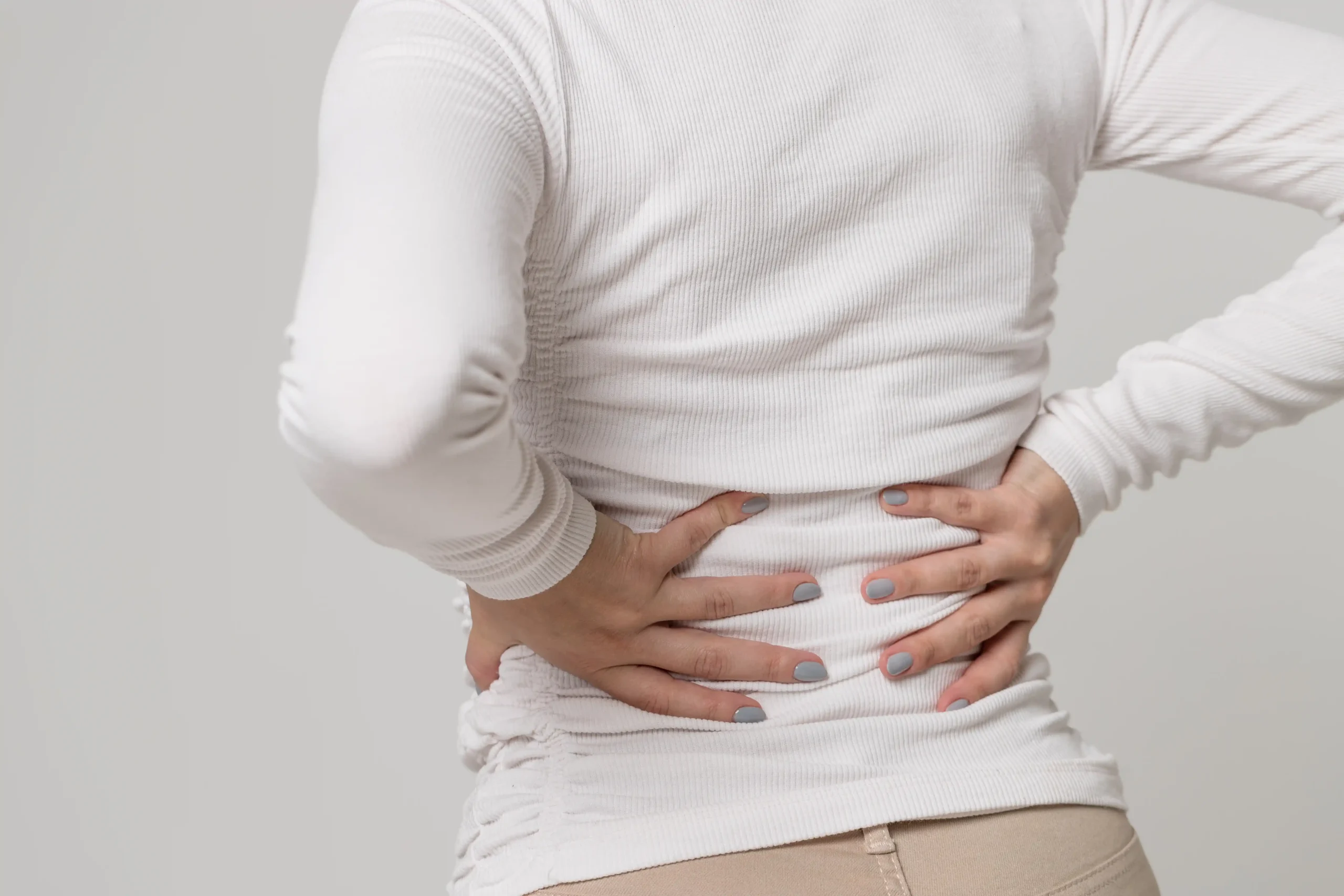 Primer plano de una mujer que sufre dolor de espalda, destacando las molestias por distensión muscular o problemas de columna relacionados con trastornos musculoesqueléticos.