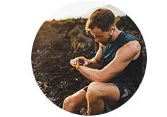 Man sitting on a rock wearing earbuds and checking his smart watch