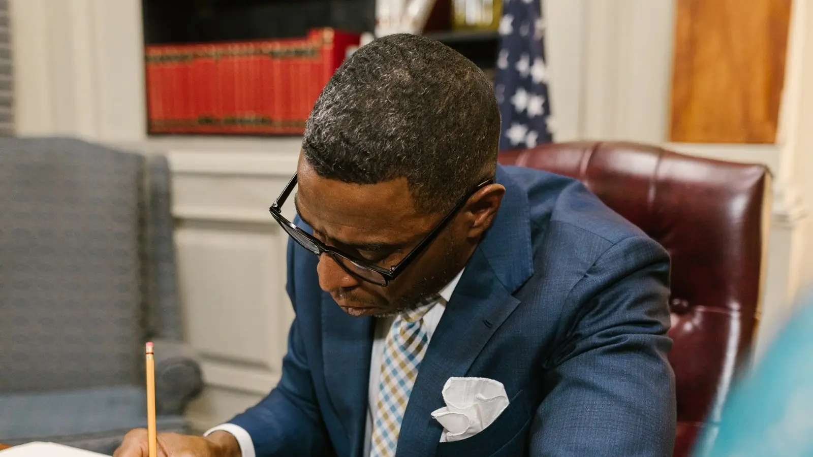 Attorney at his desk reviewing a document, law books and a flag behind him