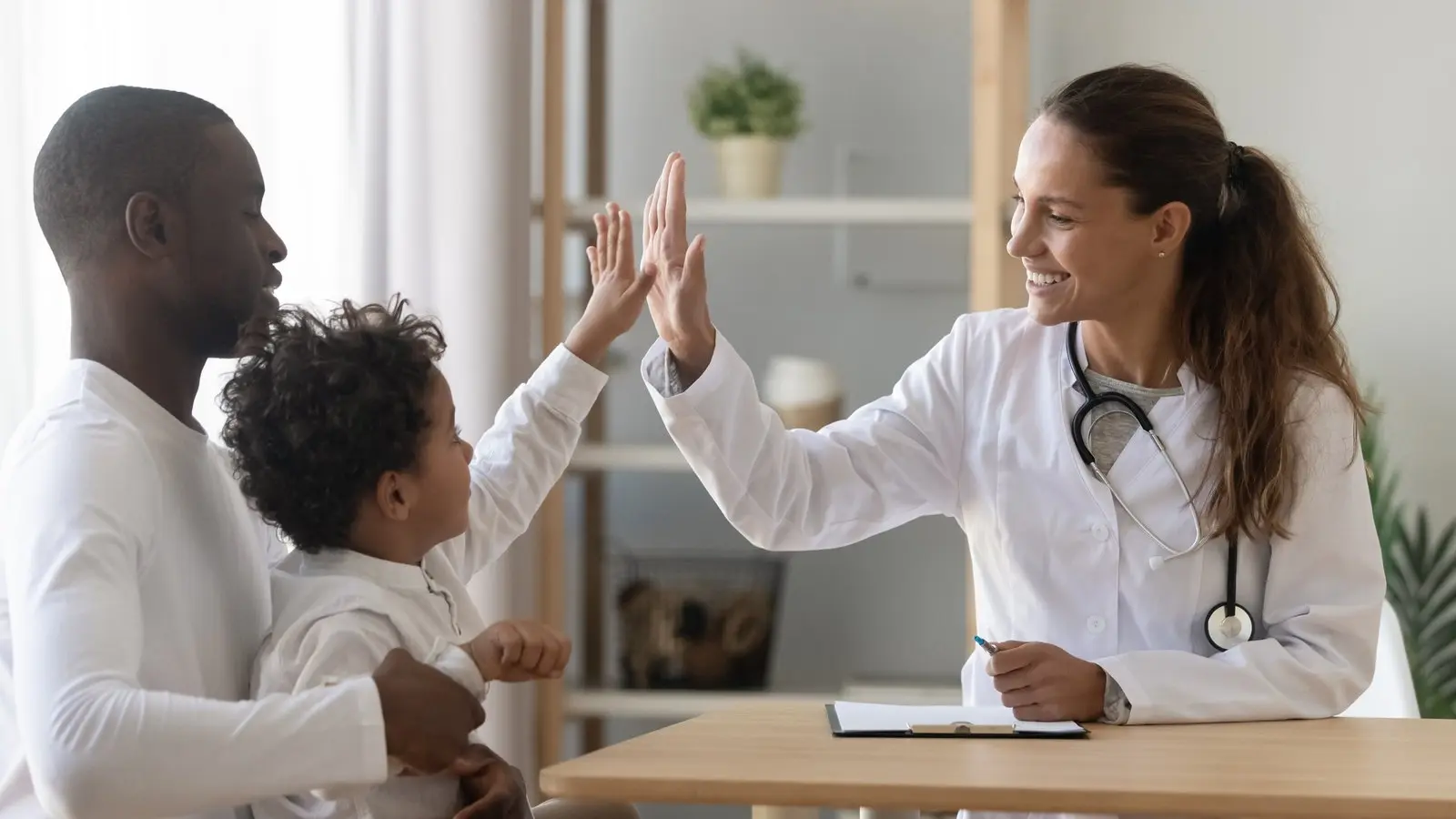 Doctor giving a young patient a high five while his father holds him