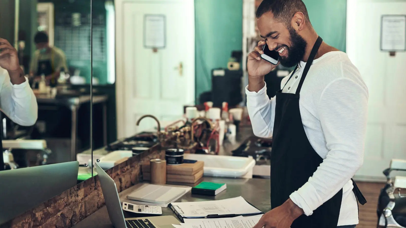 A home services owner and his office coordinator review Google Ads changes on a laptop at a wooden desk in a small contractor office, a work van visible through the window.