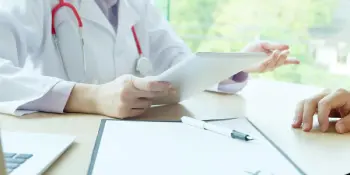 Doctor in white coat with stethoscope using tablet to discuss treatment with patient during medical consultation for car accident or workers’ compensation injury