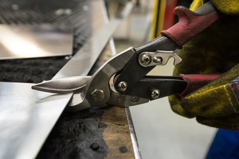 Worker using tin snips to cut metal sheet on job site