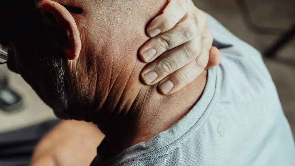 Hombre de mediana edad que se sujeta el cuello con gesto de dolor y hace muecas al tocarse el costado de la clavícula, síntoma habitual de latigazo cervical, distensión cervical o lesión de tejidos blandos tras un accidente de tráfico o un accidente laboral.