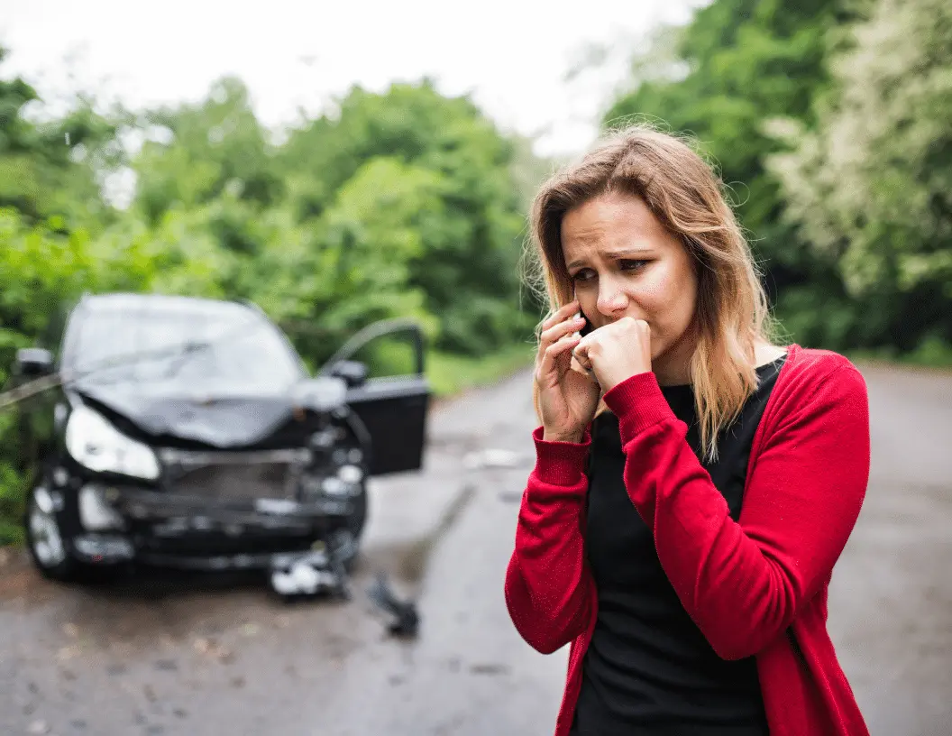 Mujer alterada hablando por teléfono junto a un coche accidentado