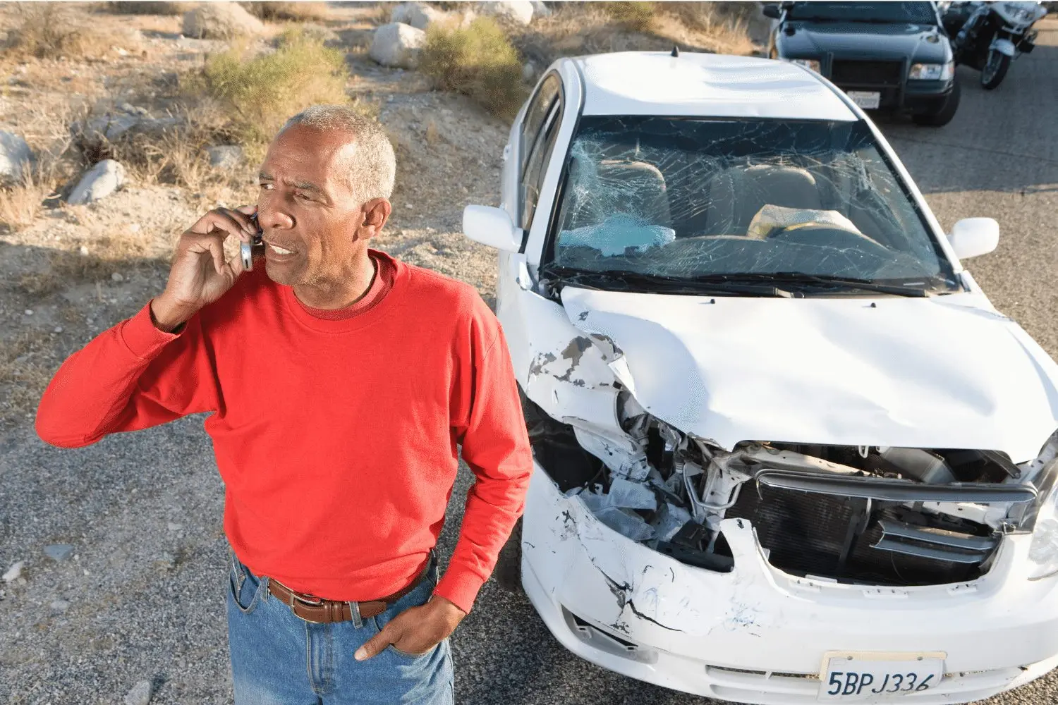 Un hombre que informa de un accidente por teléfono junto a un coche accidentado