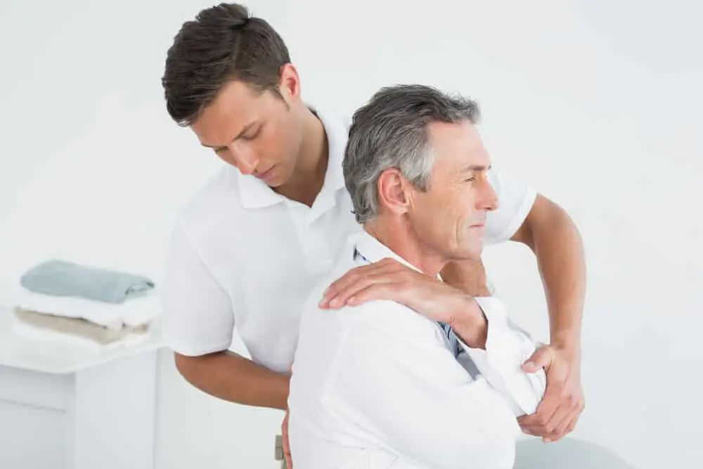 Un quiropráctico realiza un ajuste vertebral en la parte superior de la espalda y el hombro de un paciente varón de edad avanzada, tras una lesión sufrida en un accidente de tráfico, en la consulta.