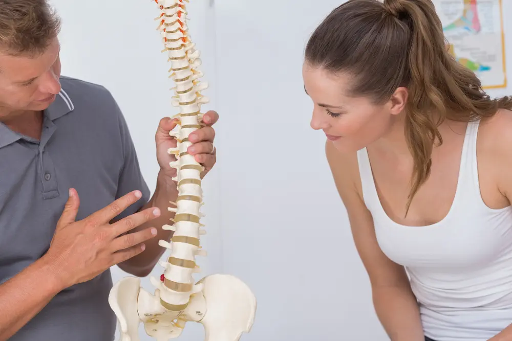 A chiropractor in Queens uses a detailed spine model to explain the source of a patient's back pain and the proposed treatment plan.