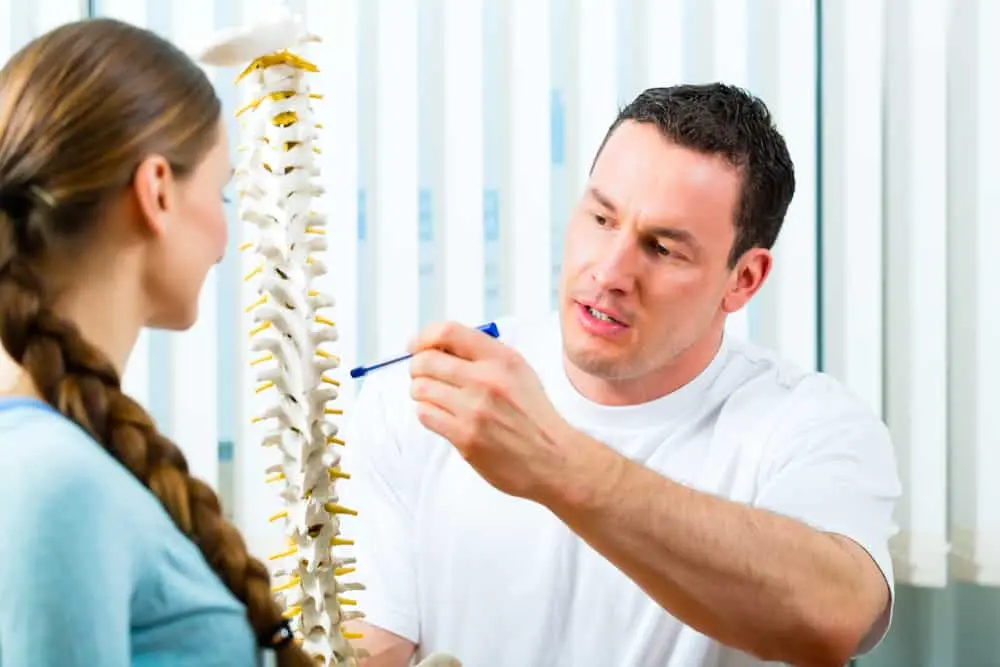 Physiotherapist in a clinic explaining a 3D model of the spine and spinal cord to a female patient to discuss spinal health and back pain care