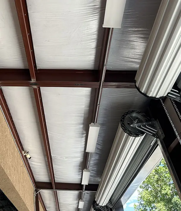 Long LED strip fixtures mounted along a brown metal ceiling frame with white insulation panels in a covered commercial area.