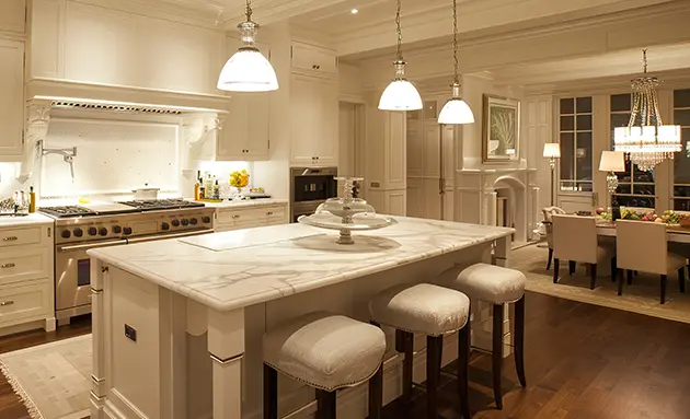 Luxury kitchen with pendant lights over a marble island, warm under-cabinet lighting, and a chandelier glowing in the adjoining dining area.