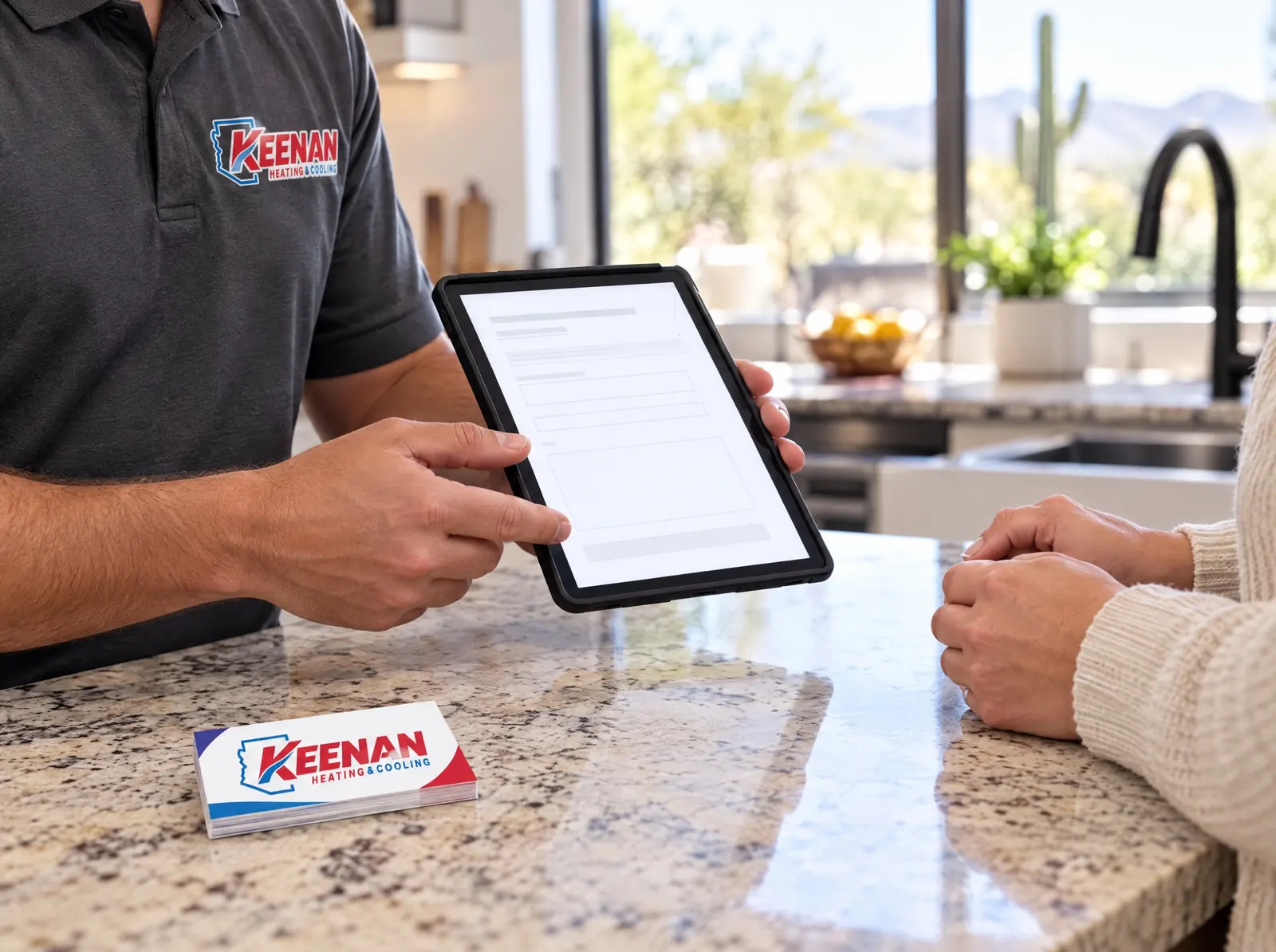 A technician in a Keenan shirt holding a tablet with a form across a kitchen counter from a homeowner