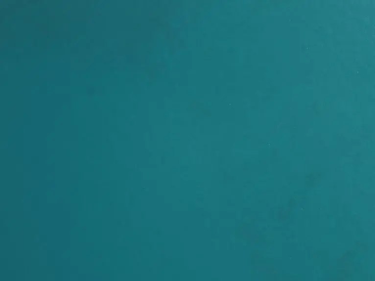 A close-up view of a textured teal surface displaying subtle variations in color and sheen, creating a visually interesting backdrop suitable for various design applications