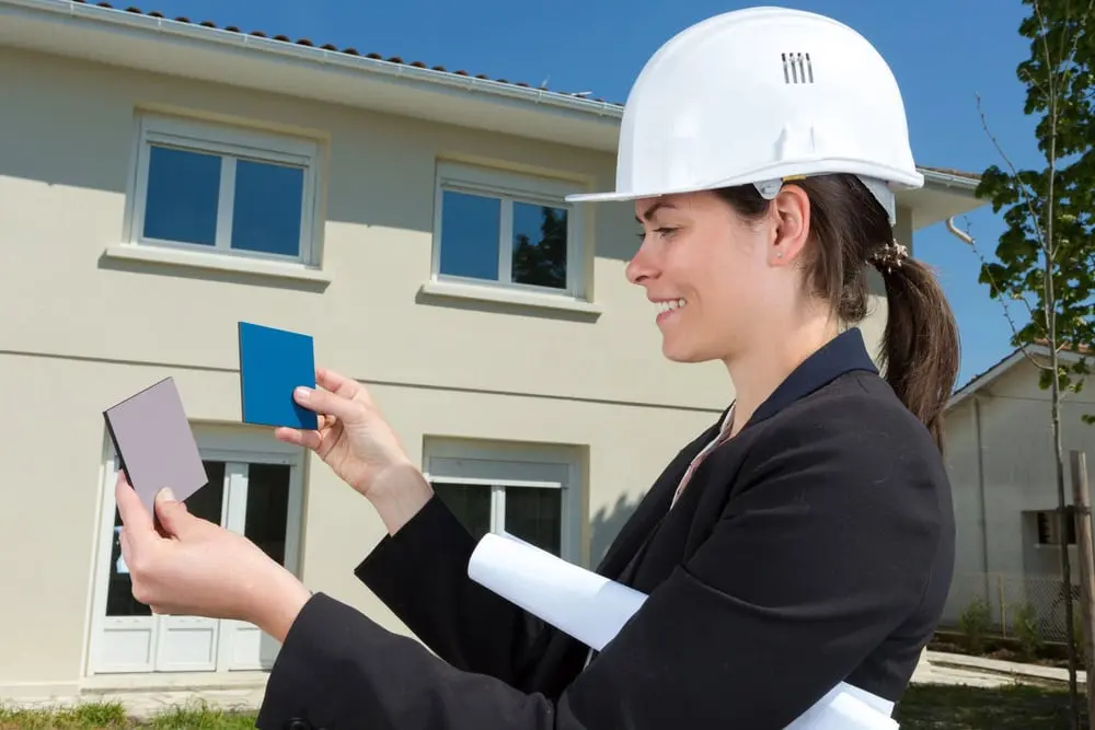 Person comparing paint color cards in front of a house